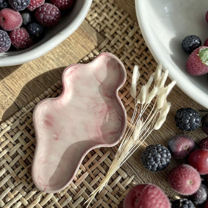 Bandeja decorativa AIKO con forma de nube irregular y acabado de mármol en tonos rosa y blanco sobre base de mimbre