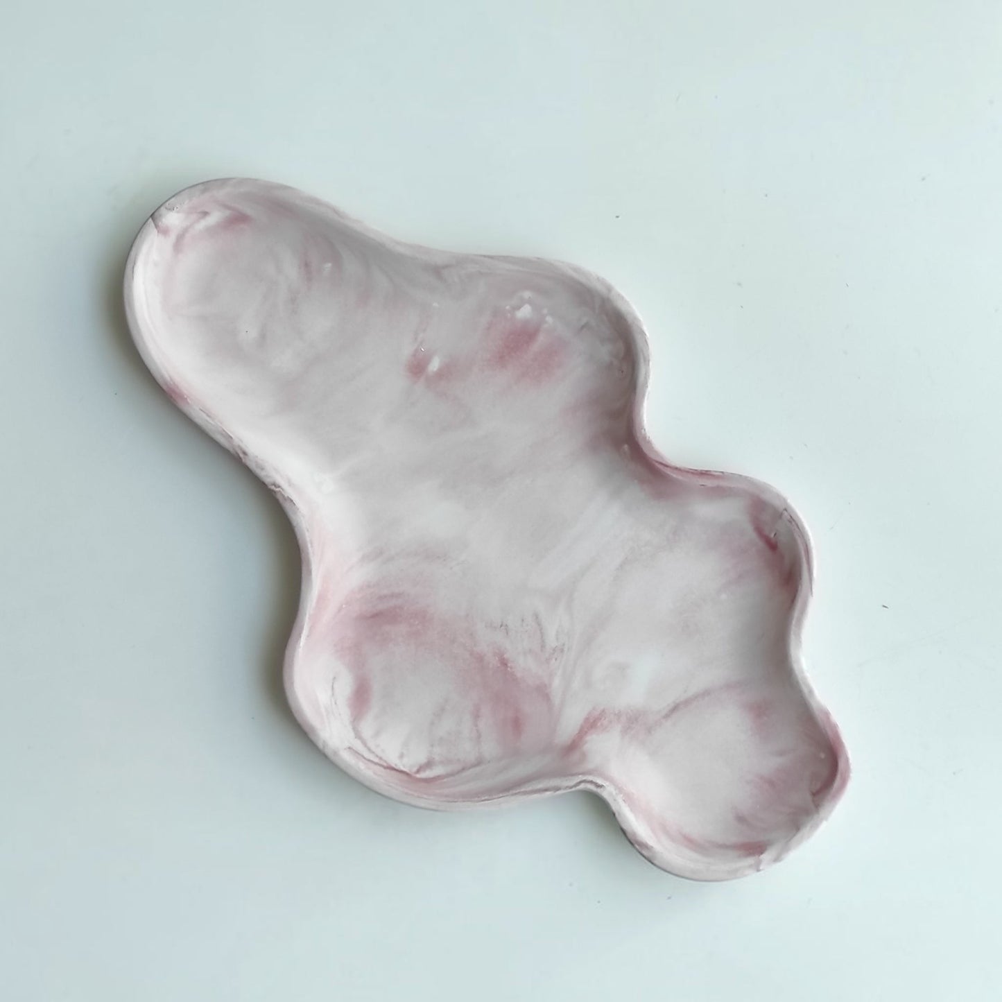 Bandeja decorativa AIKO con forma de nube irregular, fabricada en resina con acabado efecto mármol en tonos rosa y blanco.