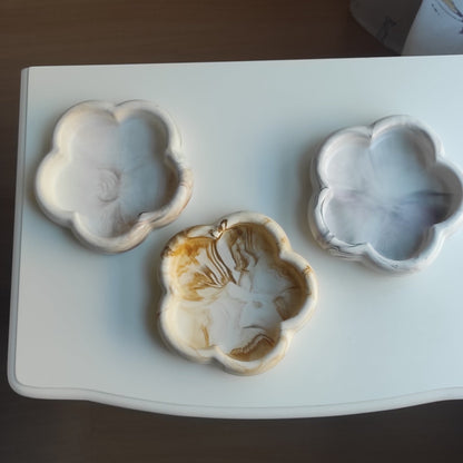 Tres bandejas decorativas AIKO con forma de flor y acabado marmolado artesanal en tonos neutros sobre mesa blanca.